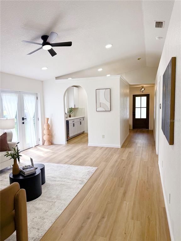 A living room with light wood floors, a ceiling fan, and an arched kitchen entryway — 1112 W 7TH STREET, SANFORD, FL