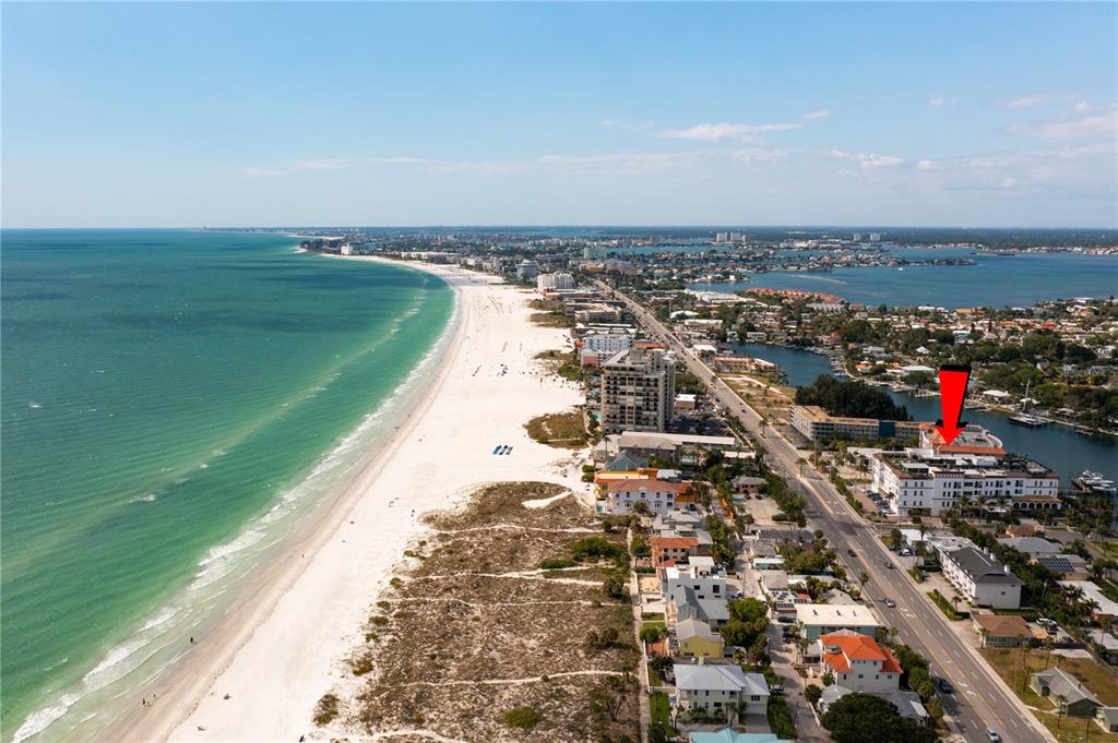 An aerial view shows a multi-story waterfront condominium building with a red arrow pointing to a balcony — 3805 GULF BOULEVARD UNIT 203, ST PETE BEACH, FL