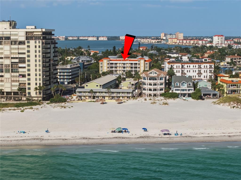 An aerial view shows a waterfront condominium complex with a pool and boat docks — 3805 GULF BOULEVARD UNIT 203, ST PETE BEACH, FL
