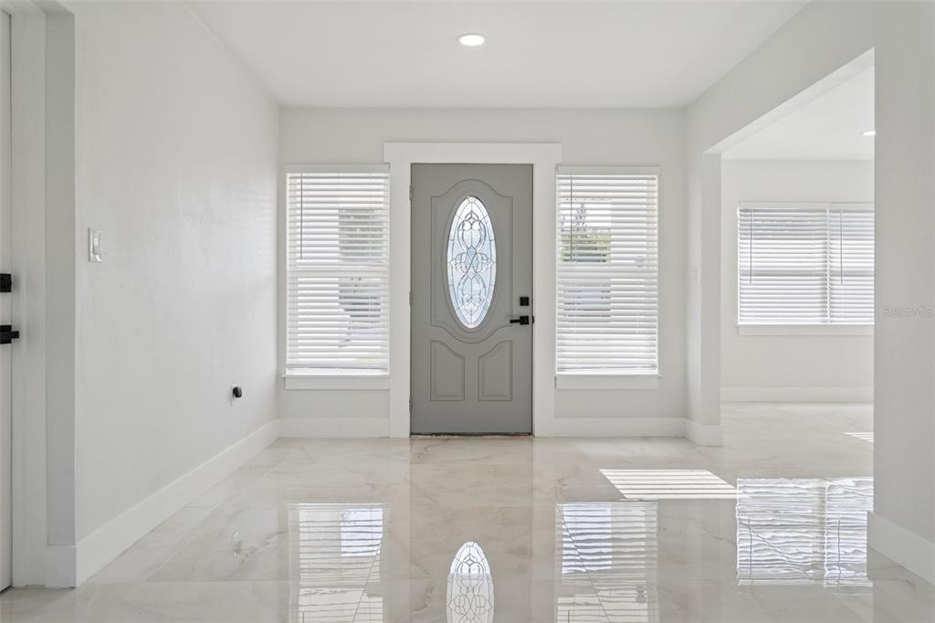 A bright entryway features a gray front door with an oval glass insert and tile flooring — 540 MILWAUKEE AVENUE, DUNEDIN, FL