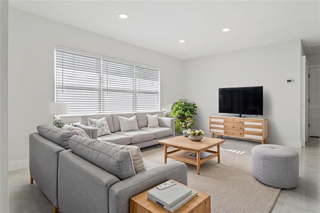 A bright living room features a grey sectional sofa, wooden coffee table, and television console — 540 MILWAUKEE AVENUE, DUNEDIN, FL