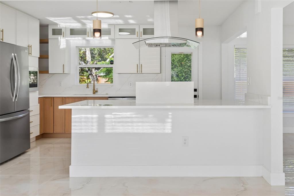 A modern kitchen features white cabinets, wood-toned lower cabinets, a white island, and stainless appliances — 540 MILWAUKEE AVENUE, DUNEDIN, FL