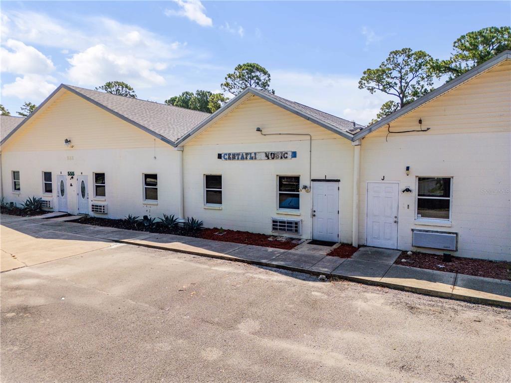 A single-story commercial building with light-colored siding, multiple entrance doors, and a paved parking lot — 555 8TH STREET UNIT I, HOLLY HILL, FL