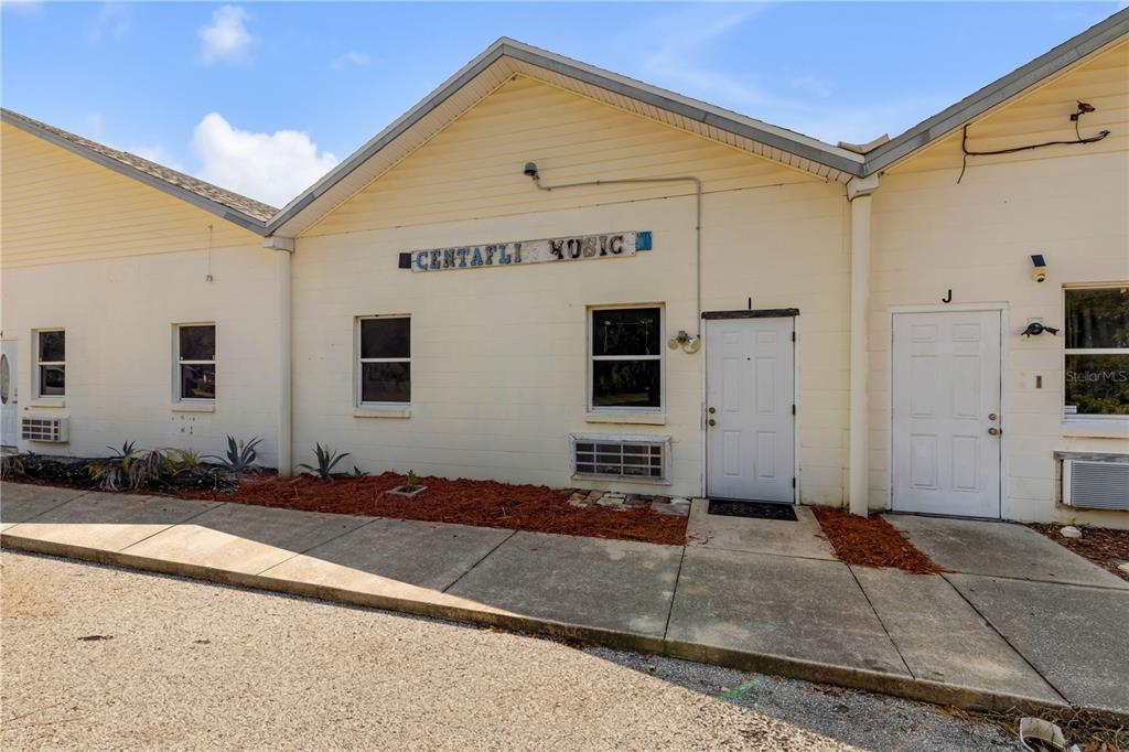 The exterior of a single-story commercial building features light-colored siding, a white door, and signage — 555 8TH STREET UNIT I, HOLLY HILL, FL