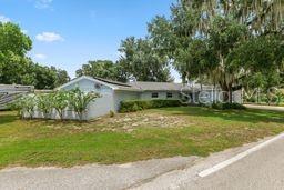 A single-story house with a white exterior and a metal roof sits behind a grassy lawn — 1901 N LAKE ELOISE DRIVE, WINTER HAVEN, FL