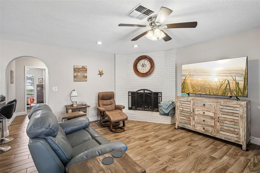 A living room features a white brick corner fireplace, wood-look flooring, and a ceiling fan — 12630 CEDAR RIDGE DRIVE, HUDSON, FL