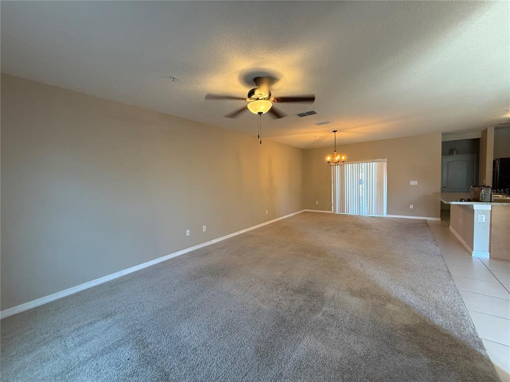 An open-concept living area features beige walls, carpeted flooring, a ceiling fan, and a chandelier — 1623 REFLECTION COVE, ST CLOUD, FL