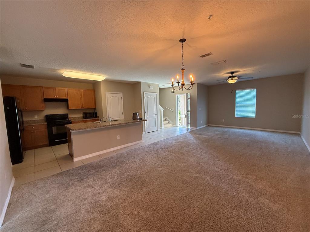 An open-concept kitchen with wood cabinets and a breakfast bar overlooks a carpeted living area — 1623 REFLECTION COVE, ST CLOUD, FL