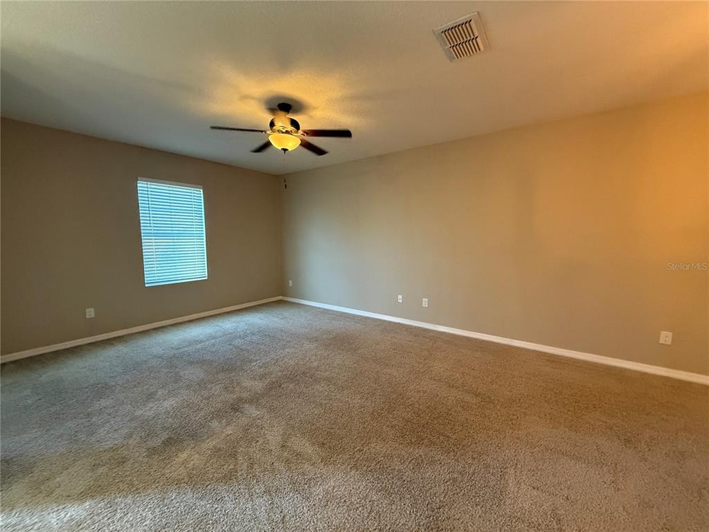 An empty bedroom features beige walls, tan carpeting, a ceiling fan, and a single window — 1623 REFLECTION COVE, ST CLOUD, FL