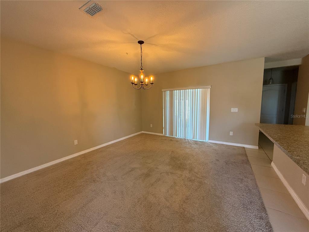 A carpeted dining area features a chandelier, beige walls, and sliding glass doors — 1623 REFLECTION COVE, ST CLOUD, FL