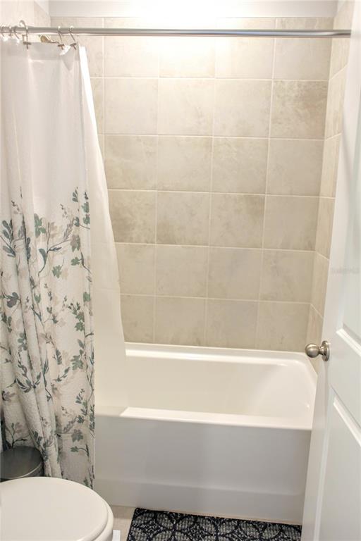 A bathroom features a white bathtub with a floral shower curtain and beige tiled walls — 2471 WARREN ACRES BOULEVARD, WESLEY CHAPEL, FL