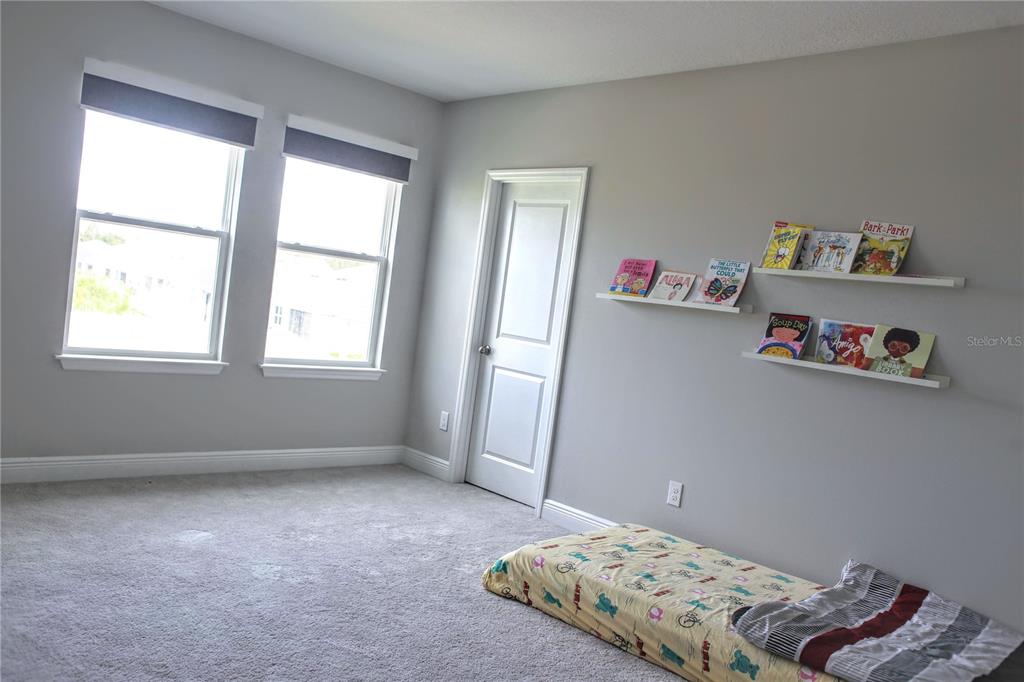 A bedroom with gray walls, carpeted flooring, two windows, a white door, and wall-mounted bookshelves — 2471 WARREN ACRES BOULEVARD, WESLEY CHAPEL, FL