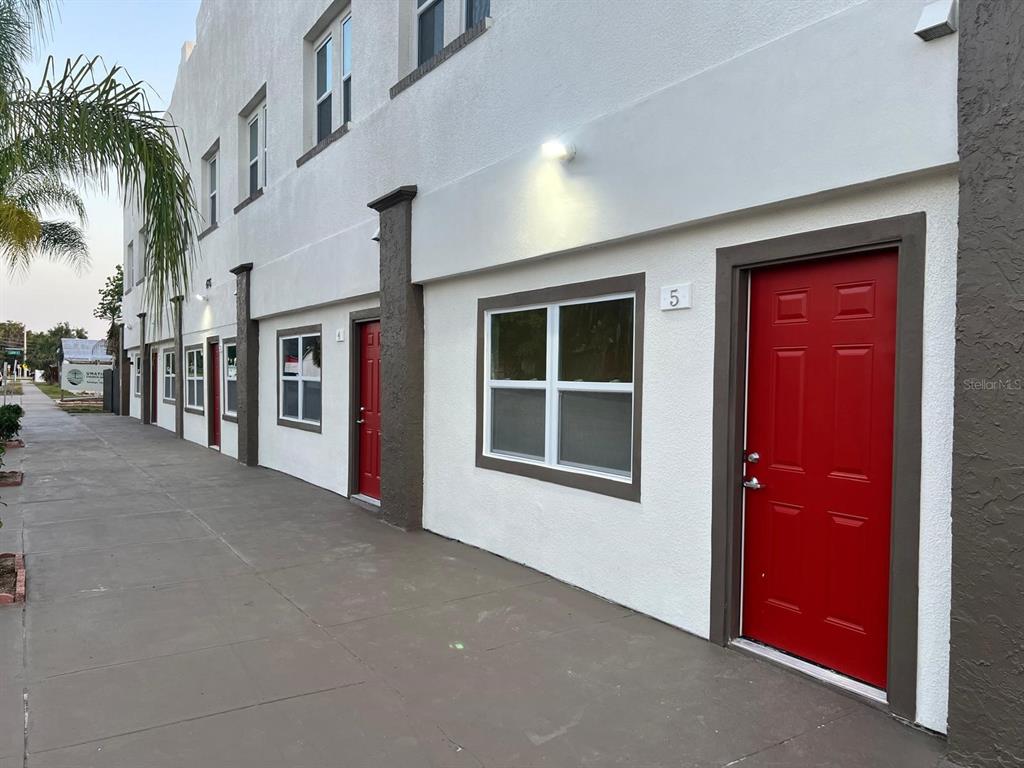 A row of white townhouses with red doors and dark trim along a concrete sidewalk — 475 UMATILLA BOULEVARD, UMATILLA, FL