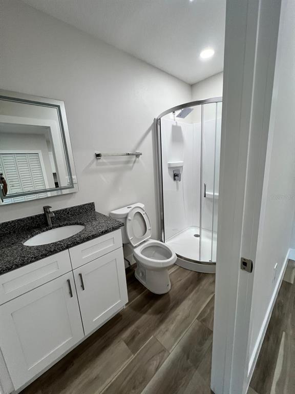 A bathroom features a white vanity with a granite countertop, a toilet, and a corner shower — 475 UMATILLA BOULEVARD, UMATILLA, FL