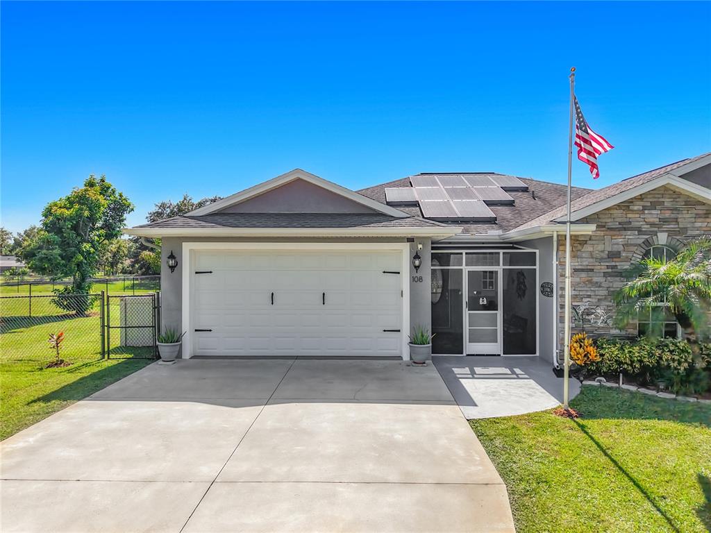 A single-story house features a two-car garage, solar panels on the roof, and a flagpole — 108 OAK KNOLLS CIRCLE, SEBRING, FL