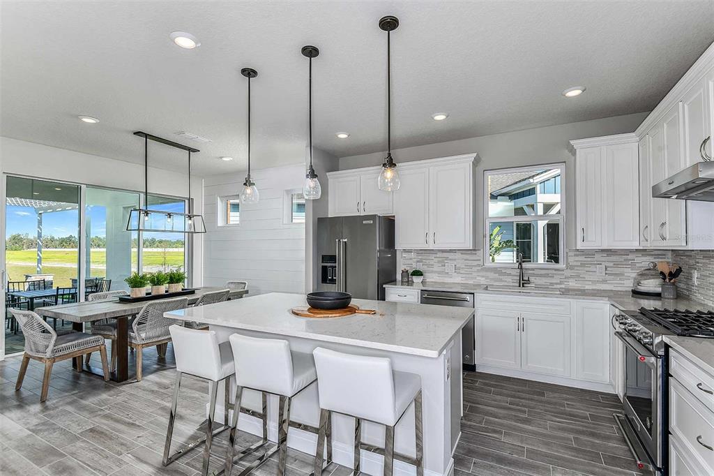 A modern kitchen features white cabinetry, a quartz island with bar seating, and gray flooring — 5038 DANCY LANE, ST CLOUD, FL
