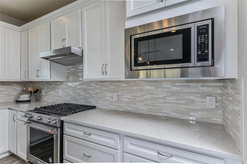 A kitchen features white cabinets, a stainless steel range and microwave, and a tiled backsplash — 5038 DANCY LANE, ST CLOUD, FL