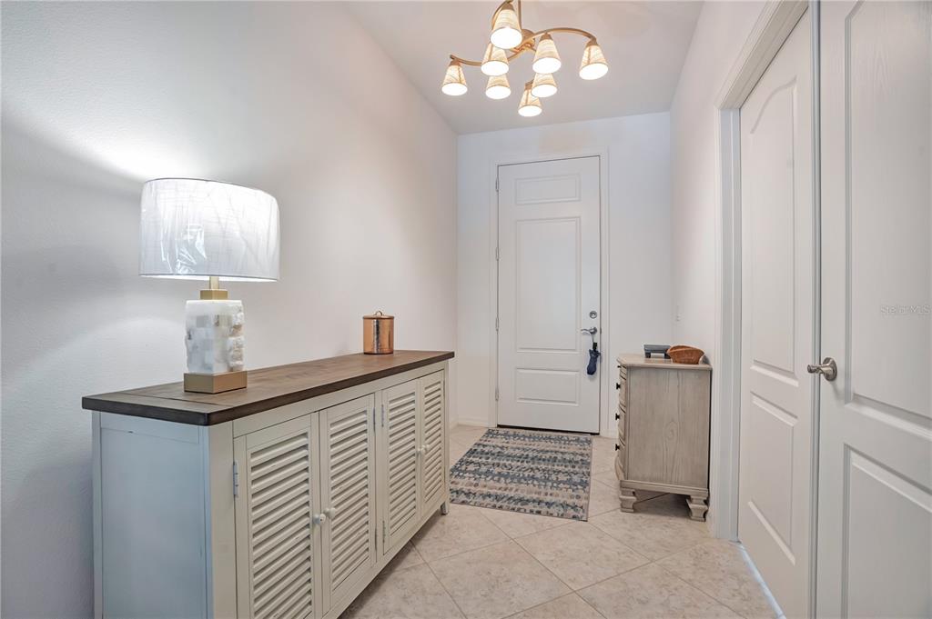 An entryway features a white door, tile flooring, a wooden console table, and a chandelier — 12225 WHISPER LAKE DRIVE, BRADENTON, FL