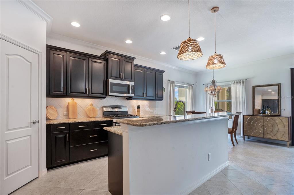 A kitchen features dark cabinetry, granite countertops, a breakfast bar, and two woven pendant lights — 12225 WHISPER LAKE DRIVE, BRADENTON, FL