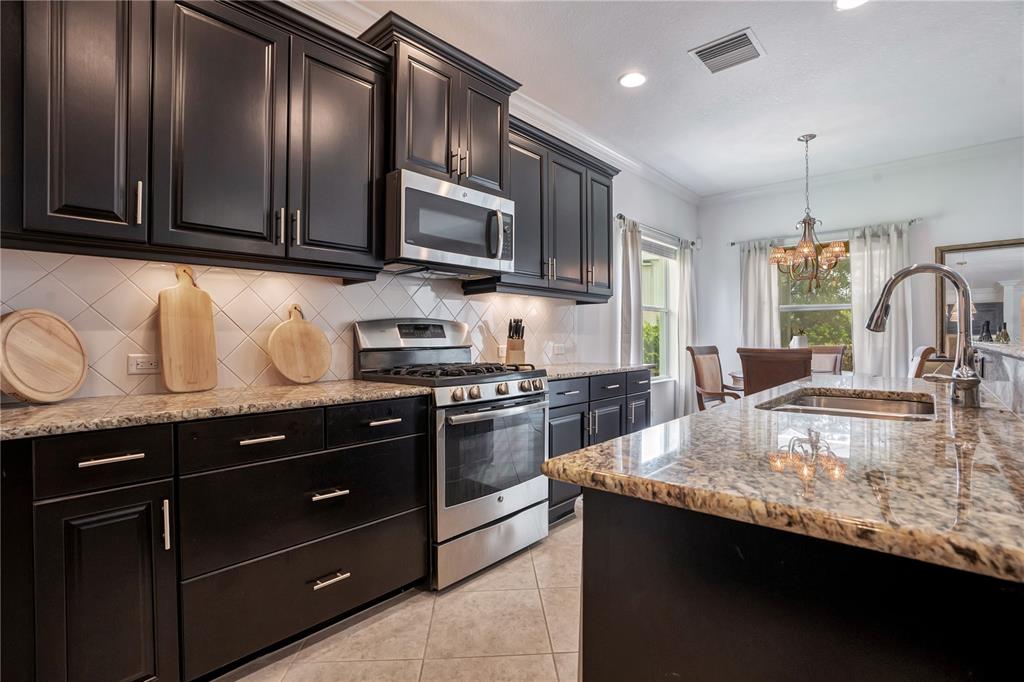 A kitchen features dark cabinetry, granite countertops, stainless steel appliances, and a central island — 12225 WHISPER LAKE DRIVE, BRADENTON, FL