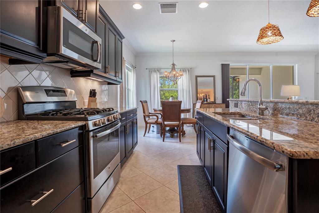 A kitchen with dark cabinets, granite countertops, stainless steel appliances, and an adjacent dining area — 12225 WHISPER LAKE DRIVE, BRADENTON, FL