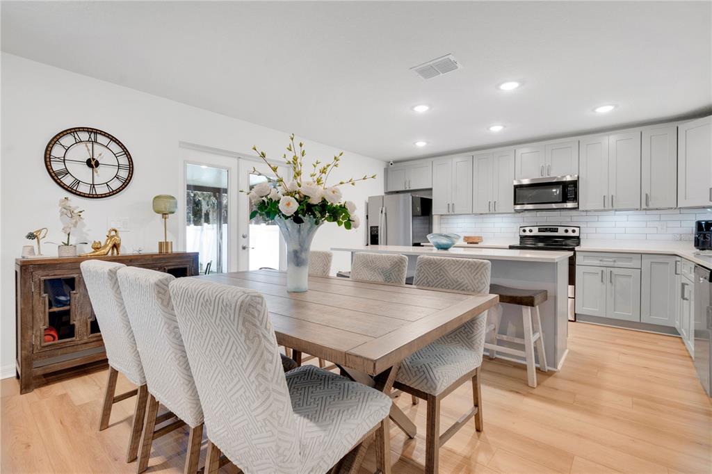 A dining area with a wooden table and patterned chairs sits before a modern kitchen — 233 E 16TH STREET, APOPKA, FL