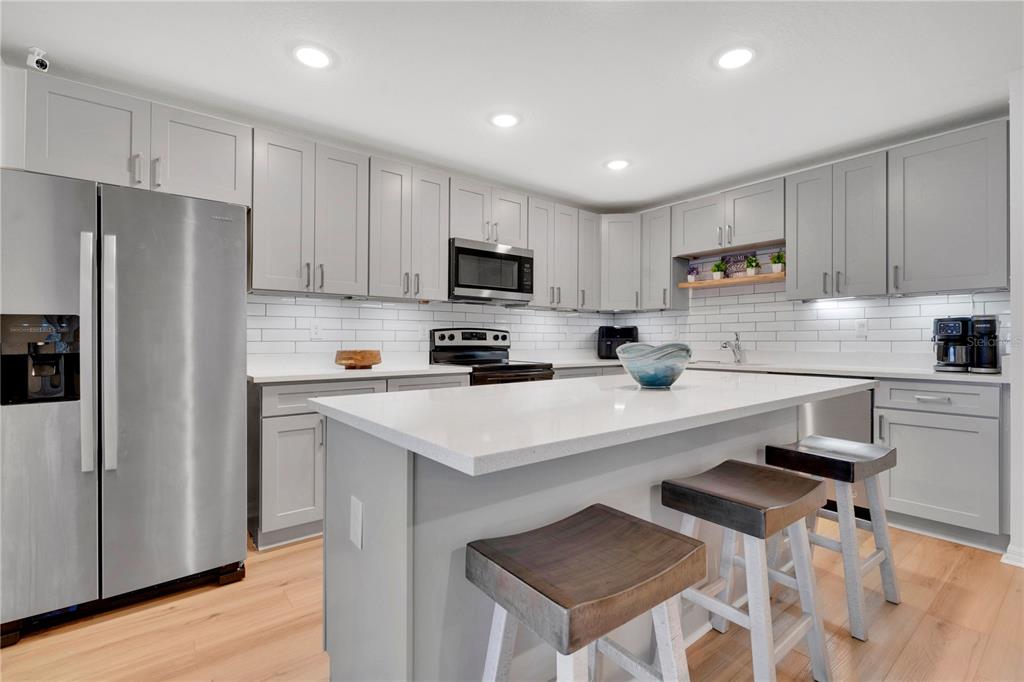 A modern kitchen features gray cabinets, white quartz countertops, a central island, and stainless appliances — 233 E 16TH STREET, APOPKA, FL