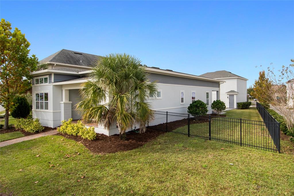 A side view of a single-story house with a palm tree and a black metal fence — 13010 STODDART AVENUE, ORLANDO, FL