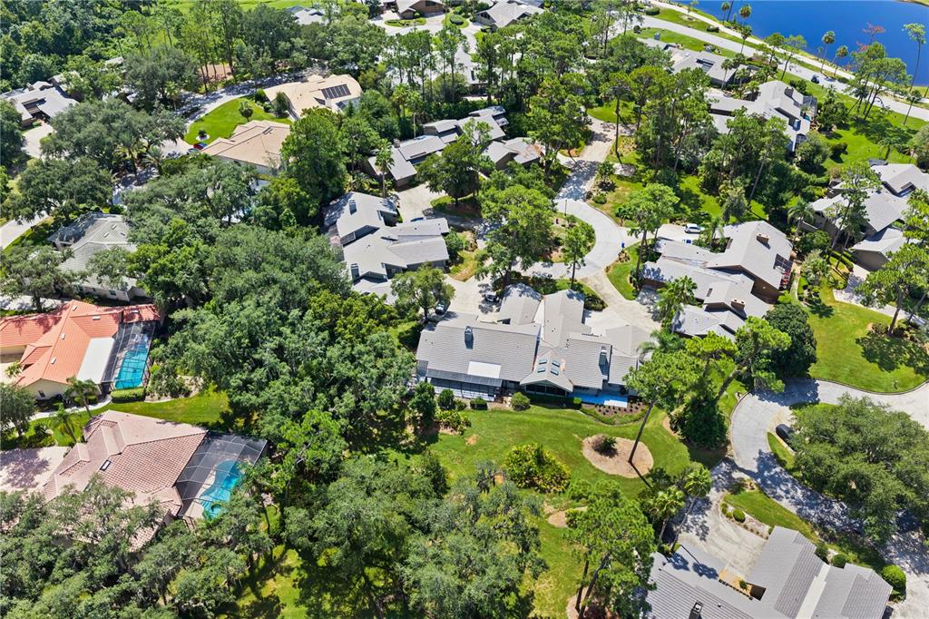 An aerial view shows multiple residential homes with gray roofs surrounded by lush green trees — 5357 COBBLESTONE COURT, WESLEY CHAPEL, FL