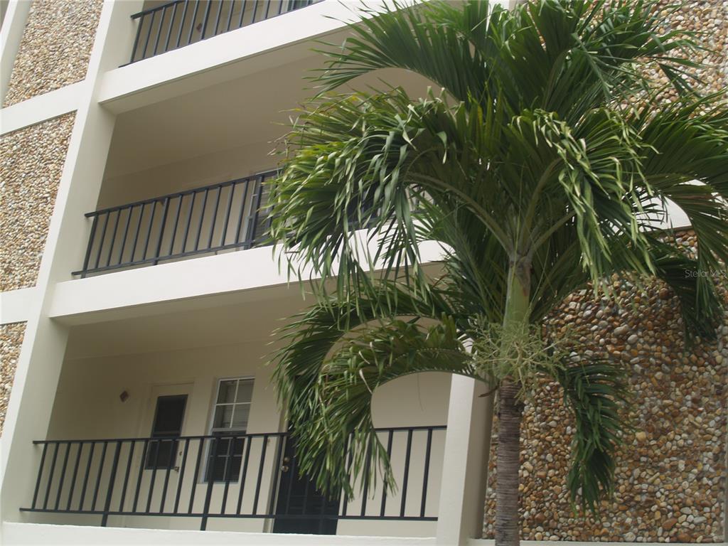 A multi-story building exterior features balconies with black railings and a textured stone wall — 7461 W COUNTRY CLUB DRIVE N UNIT 409, SARASOTA, FL