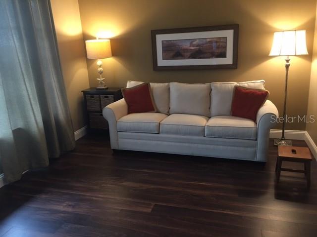 A living room features a beige sofa, two lamps, a side table, and dark wood flooring — 7461 W COUNTRY CLUB DRIVE N UNIT 409, SARASOTA, FL