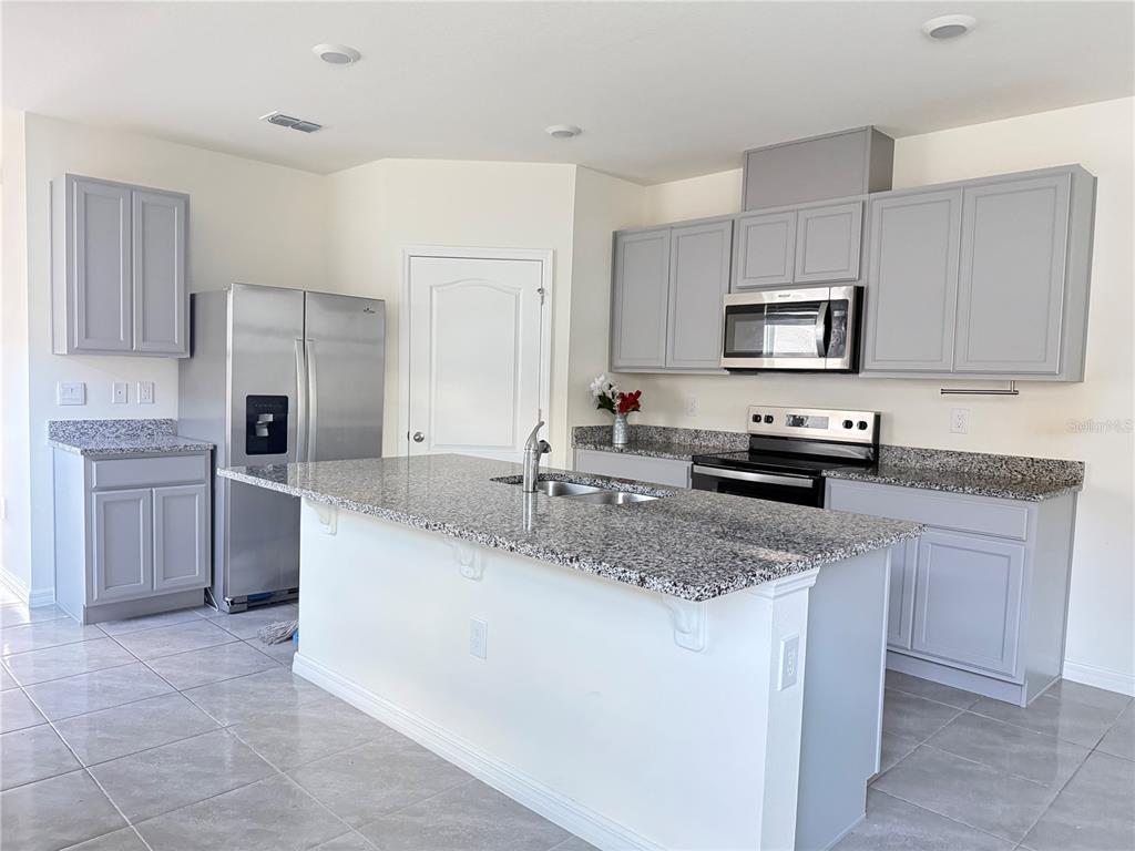 A kitchen features gray cabinets, granite countertops, stainless steel appliances, and a central island — 3732 GIORGIO DRIVE, WINTER HAVEN, FL