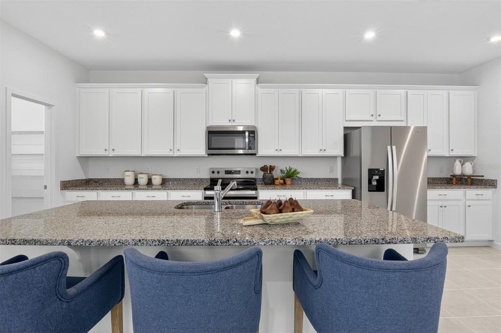 A modern kitchen features white cabinets, granite countertops, a large island, and blue bar stools — 133 GREENHOUSE GROVE STREET, GROVELAND, FL