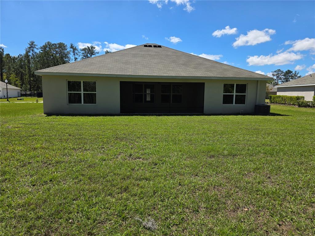 The rear exterior of a single-story house features a screened-in porch and a grassy yard — 5058 DIANTHA WAY, BROOKSVILLE, FL