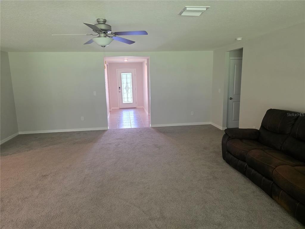 An open-concept living area features gray carpeting, a kitchen with dark cabinets, and stainless appliances — 5058 DIANTHA WAY, BROOKSVILLE, FL