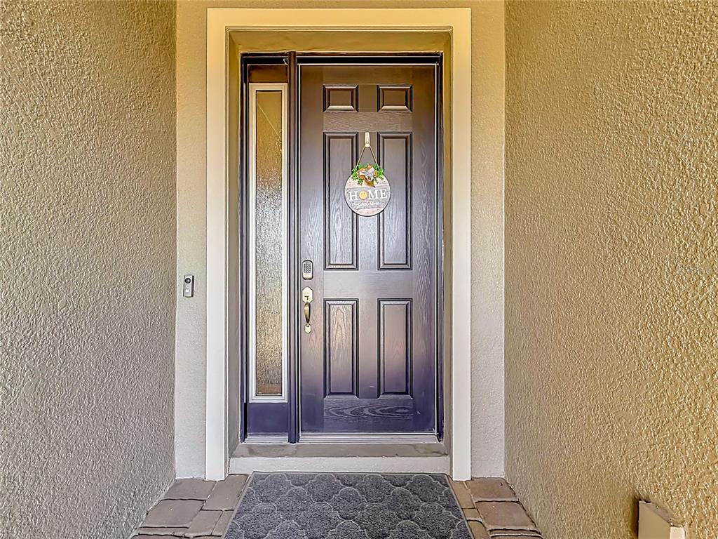 A dark front door with a side window and a welcome sign sits in an entryway — 19563 LEONARD ROAD, LUTZ, FL