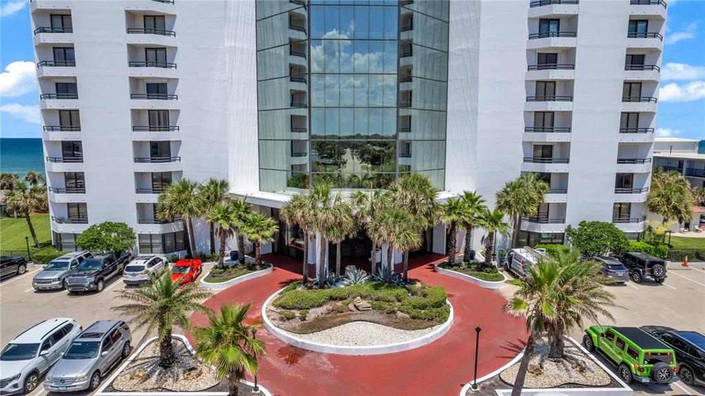 An exterior view of a multi-story white building with a circular driveway and palm trees — 2425 S ATLANTIC AVENUE UNIT 406, DAYTONA BEACH, FL