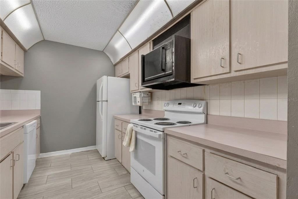 A galley-style kitchen features light wood cabinets, white appliances, and light-colored tile flooring — 1820 SW 35TH AVENUE, OCALA, FL