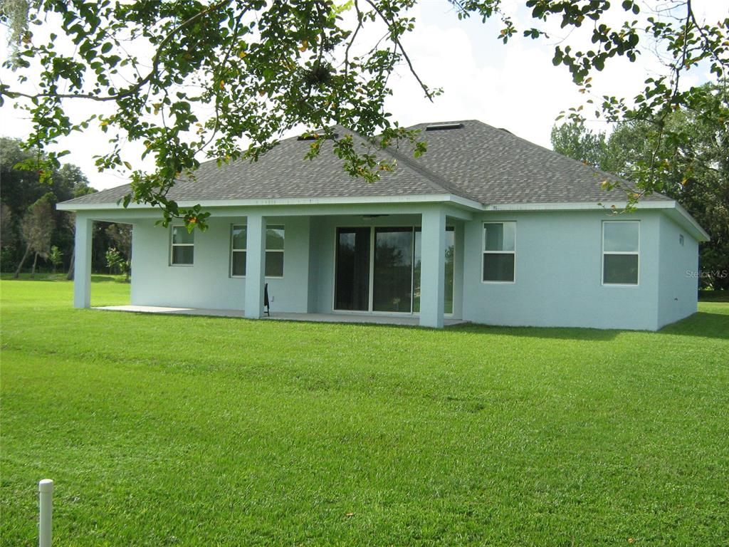 The back exterior of a light blue house features a covered patio and a large lawn — 535 DOWLING CIRCLE, LADY LAKE, FL