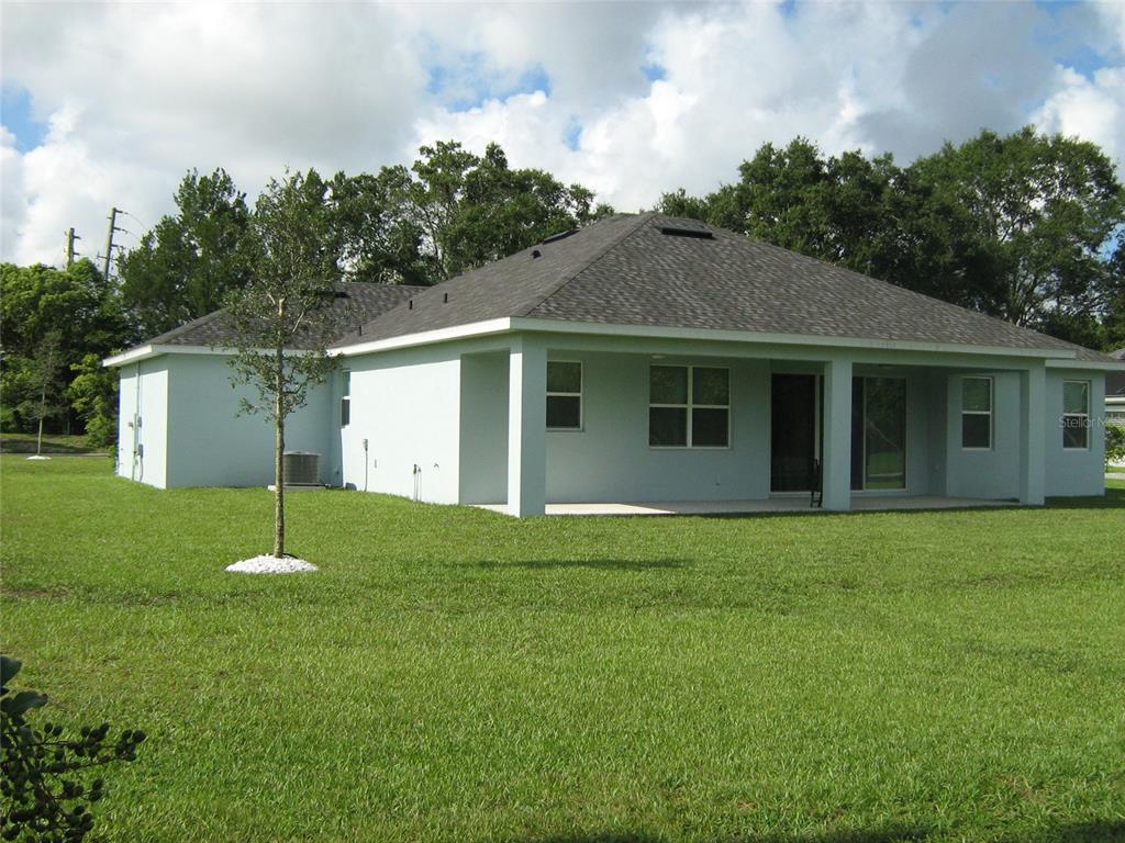 The rear exterior of a single-story house with a covered patio and a large lawn — 535 DOWLING CIRCLE, LADY LAKE, FL