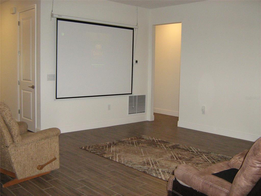 A room with wood-look tile flooring, a pull-down projector screen, and two armchairs — 535 DOWLING CIRCLE, LADY LAKE, FL