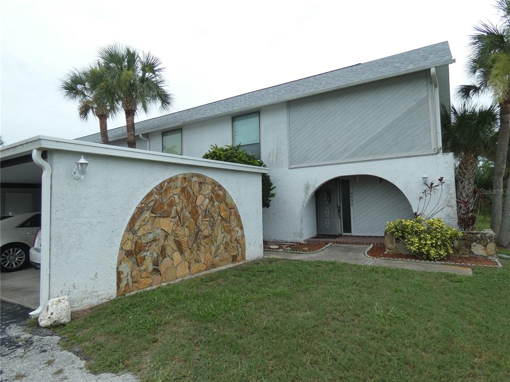 A two-story white house features a stone-accented wall, a carport, and an arched entryway — 6730 BEACH BOULEVARD, HUDSON, FL