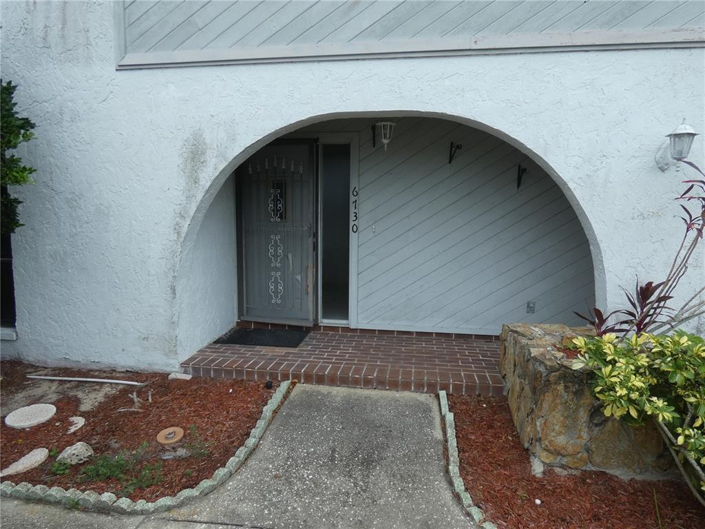 An arched entryway features a brick porch, a gray screen door, and diagonal wood siding — 6730 BEACH BOULEVARD, HUDSON, FL