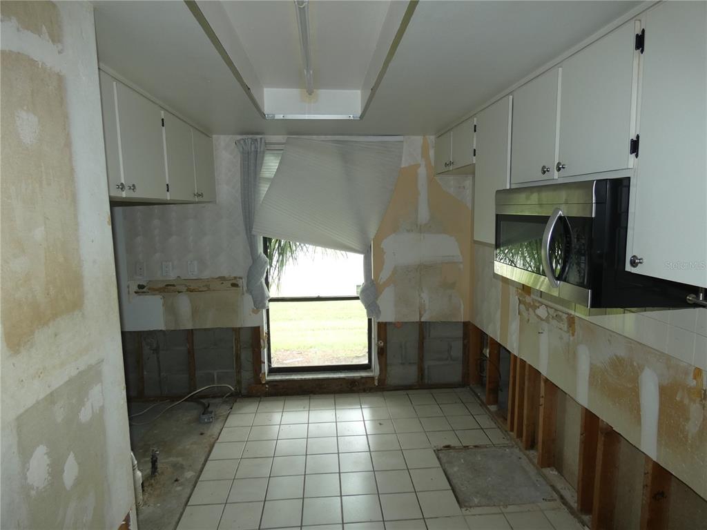 A kitchen under renovation with missing lower cabinets, exposed wall studs, and white tile flooring — 6730 BEACH BOULEVARD, HUDSON, FL