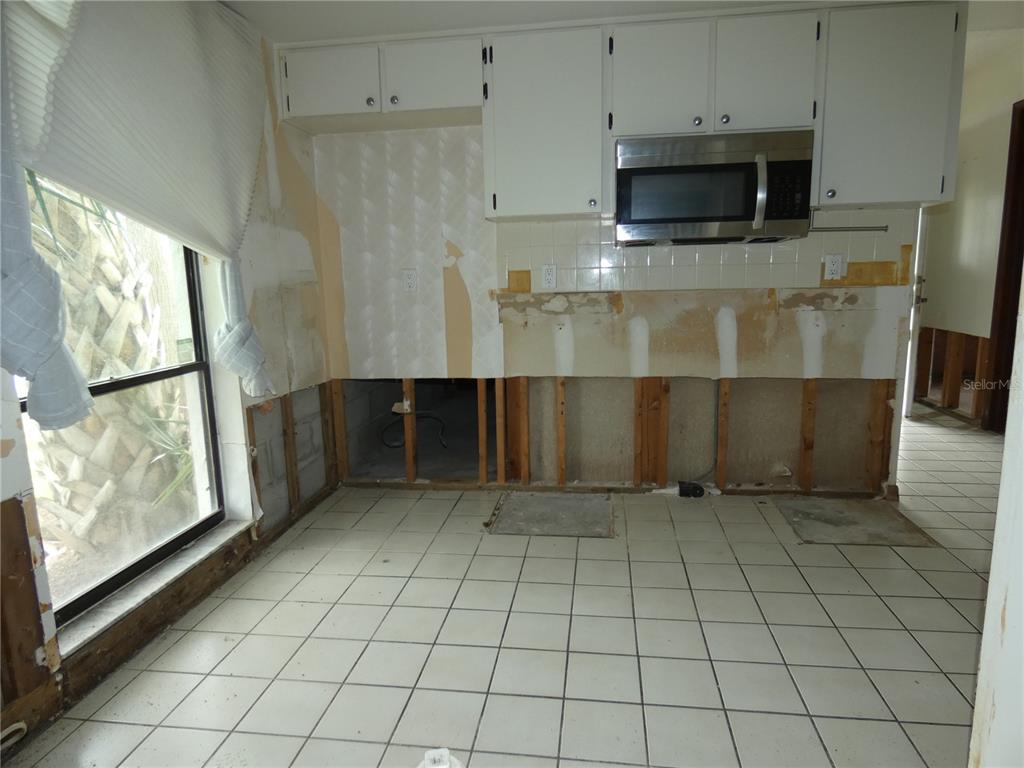 A kitchen under renovation with missing lower cabinets, exposed wall studs, and white floor tiles — 6730 BEACH BOULEVARD, HUDSON, FL