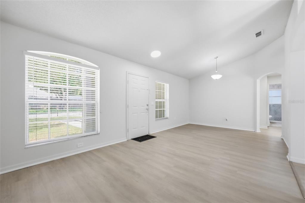 An empty living room features light-colored wood-look flooring, white walls, and a large arched window — 2706 KRIS XING, OCOEE, FL