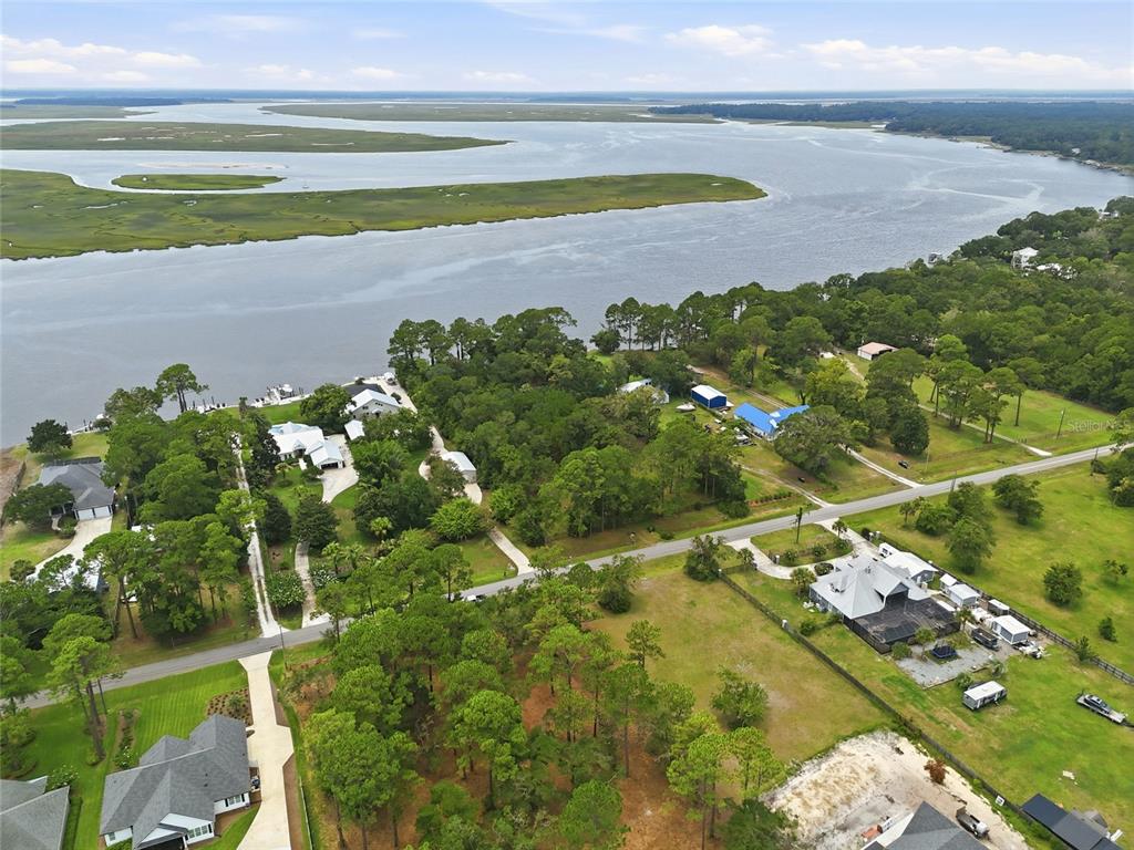 An aerial view shows houses nestled among trees along a river with marshy islands — 95289 NASSAU RIVER ROAD, FERNANDINA BEACH, FL