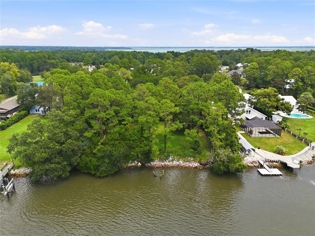 An aerial view shows a wooded waterfront lot situated between two residential properties with docks — 95289 NASSAU RIVER ROAD, FERNANDINA BEACH, FL