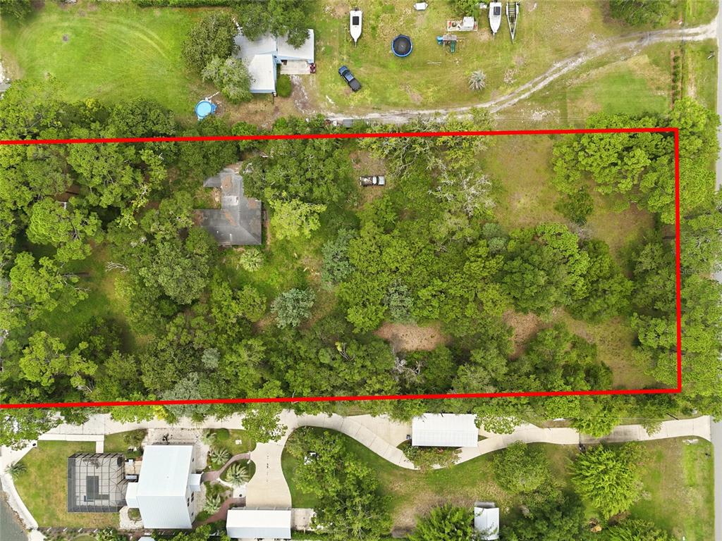 An aerial view shows a rectangular, tree-covered lot outlined in red next to residential properties — 95289 NASSAU RIVER ROAD, FERNANDINA BEACH, FL