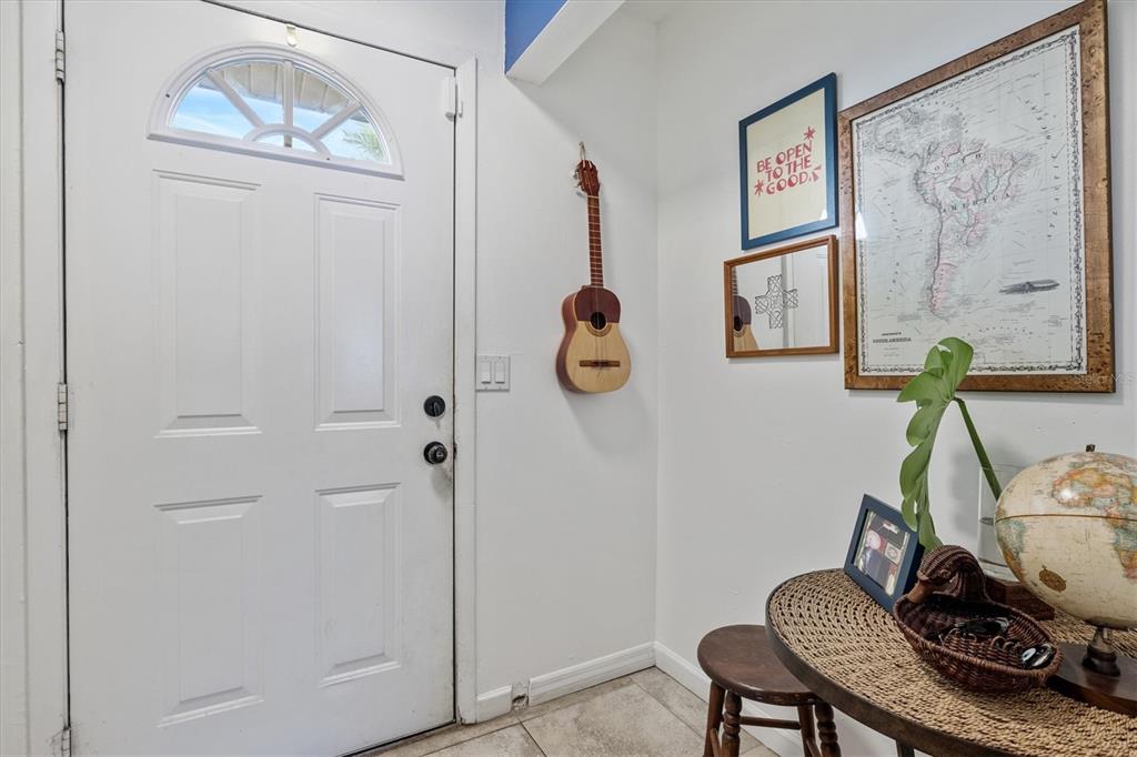 An entryway features a white front door, a wall-mounted ukulele, framed art, and a small table — 903 BYRON LANE, SARASOTA, FL